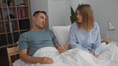 Yatak odasında erkek ve kadın tartışıyor, kapalı bir yatakta oturuyor, bir ilişki bağlamını ve duygusal iletişimi vurguluyor..