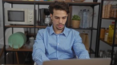 Ofiste oturan mavi gömlekli genç adam elleri yüzü kapalıyken stresli görünüyor. Etrafı raflarla çevrili. Mutfak eşyaları iş yerindeki endişeleri gösteriyor..