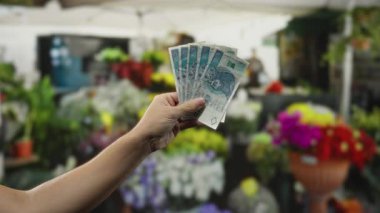 Çiçekçide elinde Polonya parası tutan adam canlı buketler ve bulanık arka planla çevrili, ticareti ve para birimini vurguluyor..