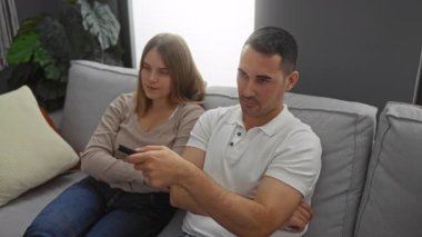 Oturma odasında rahat bir koltukta oturup uzaktan kumandayı tartışan ve evcil bir atmosferi ve canlı bitkileri olan modern bir ev ortamını tasvir eden çift.