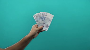 Güney Kore 'yi elinde tutan adam, izole edilmiş mavi arka plana karşı banknotlar kazandı, canlı fon üzerinden para sergiliyor, görünür erkek eli odaklı finans kavramını vurguluyor.