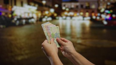 Romen leu banknotlarını elinde tutan eller seyahat sırasında bir otobüs durağında, hızlı bir şekilde para değişimi ve taşımacılığı vurguluyor.
