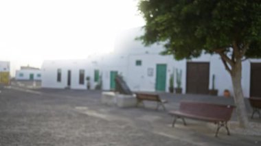 Lanzarote 'deki açık hava ortamının bulanık görüntüsü, bokeh arka planda yeşil kapıları, bankları ve ağaçları olan beyaz binaların yer aldığı İspanya