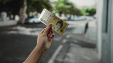 Güney Kore 'yi elinde tutan adam, bir şehir caddesinde, açık havada, şehir ortamında finansal temaları gösteren bir banknot kazandı..