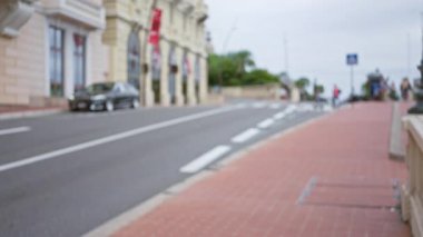 Monaco 'da bulanık yayalar ve şık bir arabayla şehir zarafetini dinamik bir bokeh etkisi altında canlı mimariyle harmanlayan sönük, lüks bir sokak sahnesi..