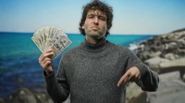 Amerikan dolarlarını elinde tutan İspanyol adam sahilin aşağısında ciddi bir ifadeyle bir sahili işaret ediyor..