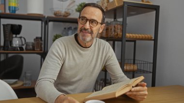 Modern ofiste kitap okuyan İspanyol bir adam, gözlük takıyor, çağdaş dekor ve düşünceli ambiyansın ortasında olgun bir yaşam tarzı sergiliyor..