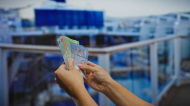 Deniz kenarı limanına bakan bir teknede Malezya bandıralı banknotlar tutan adam, açık havada mali bir alışveriş ya da iş anlaşması ima ediyor..