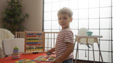 Güzel ışıklandırılmış bir anaokulu ortamında renkli ve eğitici oyuncaklarla oynayan genç sarışın çocuk.