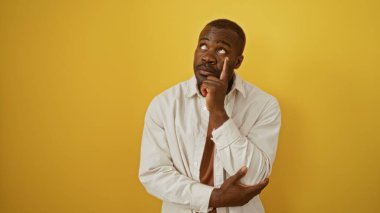 Yakışıklı, Afro-Amerikalı bir adam izole edilmiş sarı bir arka plan üzerinde düşünüyor.