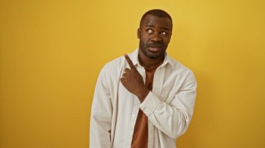 Yakışıklı Afro-Amerikalı genç adam sarı arka planda dururken işaret ediyor.