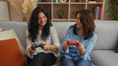 İki orta yaşlı kadın, rahat, modern bir oturma odasında oyun oynuyorlar. Kahkaha ve dostlukla dolu, rahat ve şık dekorlarla çevrili..