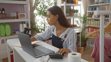 Ev dekorasyonu mağazasında çalışan genç bir kadın dizüstü bilgisayarına odaklanmış durumda..