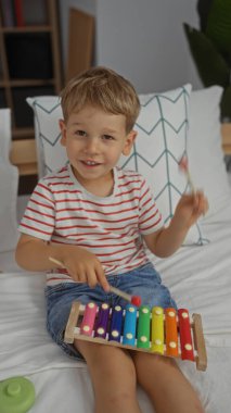 Şirin sarışın çocuk, rahat bir yatak odasında, renkli bir ksilofon çalıyor. İçerideki çocukluk sevincini gösteriyor..