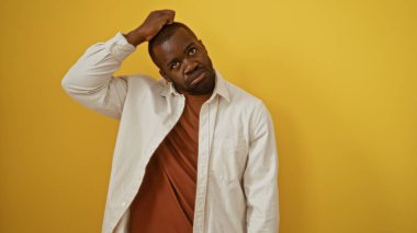 Genç Afro-Amerikan erkeği elini başının üstüne koyup parlak sarı bir arka plana karşı düşünceli görünüyor çarpıcı ve içsel bir görüntü yaratıyor..