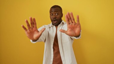 İzole edilmiş sarı bir arka planda el kol hareketi yapan genç adam şaşırdığını ve odaklandığını ifade ediyor..