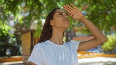 Güneşli bir günde şehir parkında güneş ışığından gözlerini gölgeleyen kadın