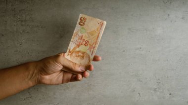 Elle tutulan Türk lirası, beton bir arka planda, 50 lira banknot gösteriyor..
