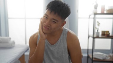 Sağlık spa odasında yakışıklı genç bir adam. Rahatlatıcı bir güzellik seansı sırasında gülümsüyor ve nazikçe yüzüne dokunuyor.