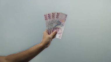 İzole edilmiş beyaz arkaplan üzerinde Türk lirası banknotları tutan adam, açık ve minimalist bir ortamda para birimi detayları ve ekonomik konsept sergiliyor.