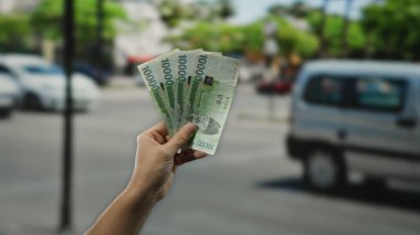 Güney Kore 'yi elinde tutan adam, şehir trafiği ve açık hava manzarasıyla çevrili işlek bir caddede, modern finansal refahı simgeleyen banknotlar kazandı..