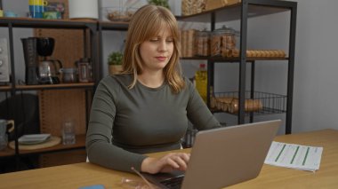 Ofis ortamında dizüstü bilgisayar ve modern dekorlarla çalışan bir kadın, kapalı alanda üretken bir çalışma ortamı sergiliyor..