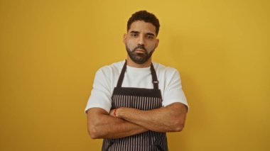 Beyaz gömlekli ve önlüklü yakışıklı genç adam izole edilmiş sarı arka planda kolları bağlı duruyor.