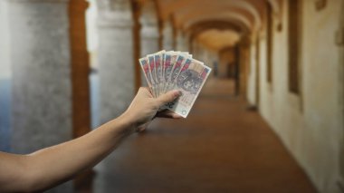 Eski bir üniversite binasının yanında elinde Polonya parası tutan bir adam tarihi bir akademik ortamda para sergiliyor..