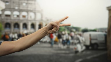Roma 'daki ikonik Roma kolezyumunun önünde barış işareti gösteren bir adam şehir hayatının ve tarihsel mimarinin özünü yakalıyor..