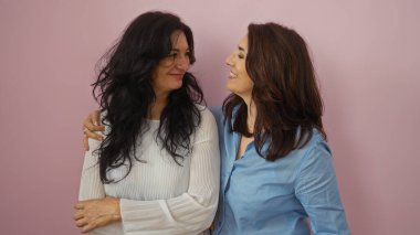 İzole edilmiş pembe duvarın üzerinde birlikte gülümseyen kadınlar, iki orta yaşlı kız kardeşle arkadaşlığı ve aileyi yakalıyorlar. Birbirlerine bağlılıklarını yansıtan huzurlu bir ortamda birbirlerine sevgiyle sarılıyorlar..