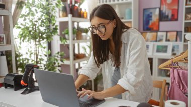 Dekorasyon ve ev bitkileriyle çevrili bir mağazada dizüstü bilgisayarda çalışan genç bir kadın.