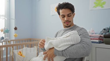 Genç İspanyol bir adam rahat bir yatak odasında bebek beşiği yapıyor. Yumuşak etkileşim ve sakin bir iç mekan havası sergiliyor..