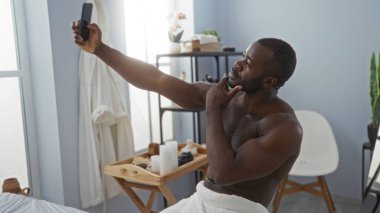 Yakışıklı genç bir adam spa sağlık merkezinde selfie çekiyor, arka planda güzellik ürünleri olan sakin bir kapalı mekan ortamı sergiliyor.