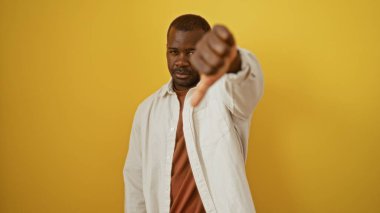 Yakışıklı, Afro-Amerikalı bir adam izole edilmiş sarı bir arka plana poz veriyor. Ciddi bir ifade ve küçümseyici bir jest.