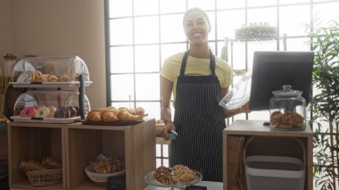 Fırın tezgahında çalışan genç bir kadın, çeşitli hamur işleri ve tatlılarla, kapalı bir ortamda, parlak ışıklandırmayla gülümsüyor..