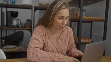 Ofis ortamında dizüstü bilgisayarda çalışan bir kadın, odaklanmış konsantrasyon ve üretkenlik sergiliyor, raflar ve modern iç mekan ile çevrili..