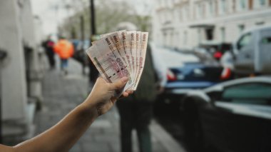 Kalabalık bir şehir caddesinde Suudi riyal banknotları tutan bir adam. Arka planda arabaları ve insanları olan, açık havada kentsel faaliyetler sergileyen bir adam..