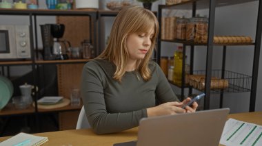 Ofiste çalışan bir kadın dizüstü bilgisayarla masa başında çalışırken raflarla ve iş yeriyle çevrili bir yerde modern, üretken bir ortam izlenimi uyandırıyor..