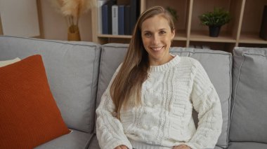 Oturma odasındaki rahat koltukta rahat bir şekilde uzanan, ahşap raflarla gülümseyen bir kadın..