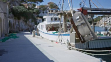 Mallorca 'daki Cala figera limanına kenetlenmiş teknelerin bulanık görüntüsü, dağılmış arka planı kıyı manzarasını ve güneş ışığı altında deniz elementlerini gösteriyor.