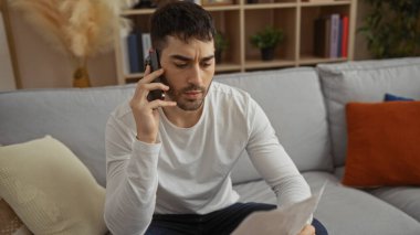 Oturma odasında telefonla konuşan genç adam, modern dekorlu, düşünceli ve odaklanmış bir iç mekan ayarını yansıtıyor..