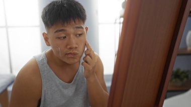 Kaplıca odasında cilt kremi süren genç bir adam. Rutin cilt bakımına ve özgüvenine odaklanıyor. Sağlık ve güzelliği yansıtıyor..