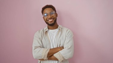Kollarını kavuşturmuş gülümseyen genç bir adam soyutlanmış pembe bir arka plana karşı duruyor, mutluluğu ve güveni somutlaştırıyor..