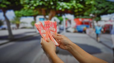 Bir şehir caddesinde renkli Filipin pesolarını tutan eller, açık bir şehir ortamında döviz ve mali faaliyetleri vurguluyor.