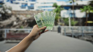 Bir şehir caddesinde Norveç kronu banknotları tutan bir adam, iş ya da finansal konsept için bulanık bir geçmişe sahip açık bir şehir ortamında para gösteriyor.
