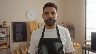 Fırında duran yakışıklı genç adam önlük giyiyordu. Arka planda ekmek ve pastalar vardı. Kapalı bir dükkanın duvarında saati vardı.