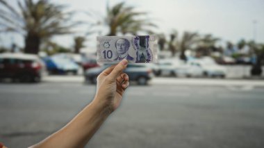 Şehir caddesinde elinde Kanada Doları banknotları tutan adam arka planda bulanık arabalarla canlı şehir ortamında para gösteriyor..