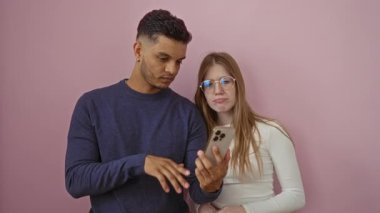 Erkek ve kadın gülümserken pembe duvara karşı akıllı telefonu işaret ederek olumlu etkileşim ve içerik onayı gösteriyor.