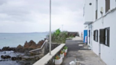 Lanzarote, İspanya 'da bulanık sahil yolu. Odaklanamayan beyaz evler, kayalık kıyı şeridi ve bulutlu gökyüzü.