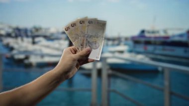 Deniz kenarındaki Türk banknotları, açık mavi gökyüzünün altında tekneler, para, seyahat ve deniz temalarını ön plana çıkarıyor..